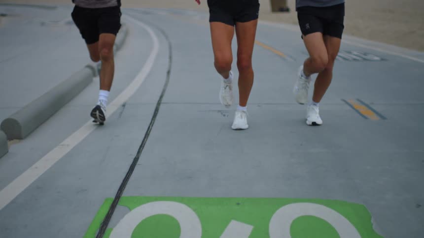 Three people two young men and one woman running side by side in the middle of the road at midday all wearing white sneakers