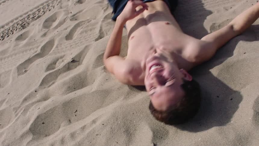 Man lying down rolling in the sand on the beach