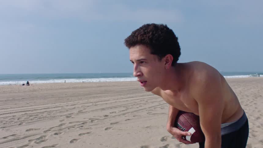 Young man stands on the beach holding a football
