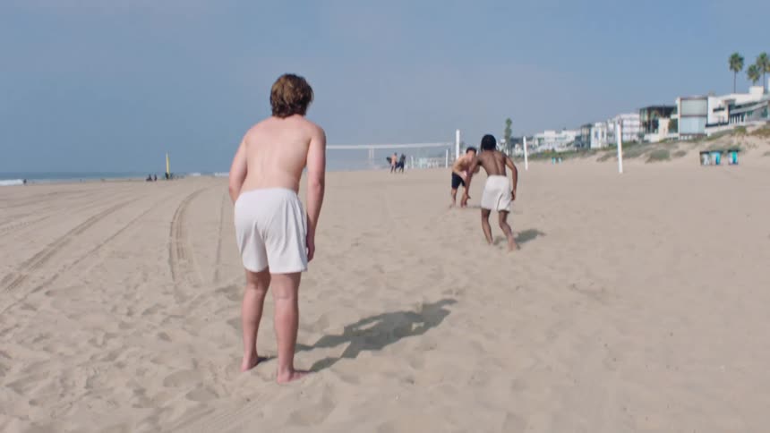 Three men playing american football on the beach