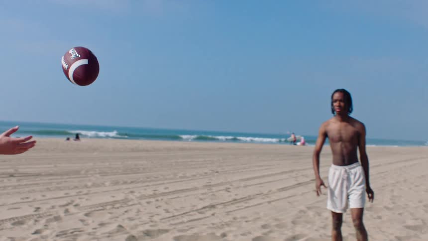 Group of three men playing american football on the beach sand