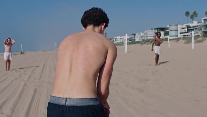 Man receiving an american football with his friends on the beach