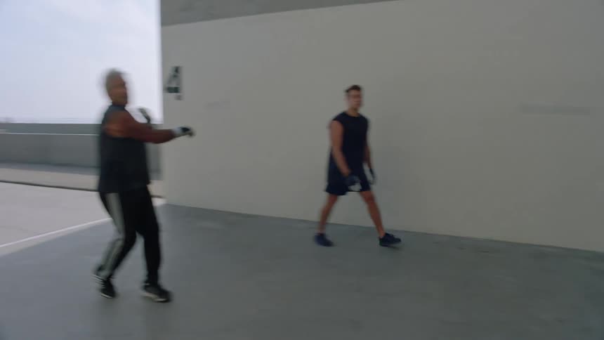 Two men wearing gloves hitting a small ball against a white wall