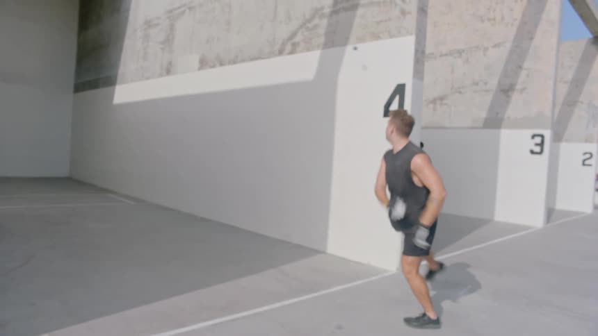 Two men are playing handball on an outdoor court with large numbered walls with one man running and preparing to hit the ball against wall number four