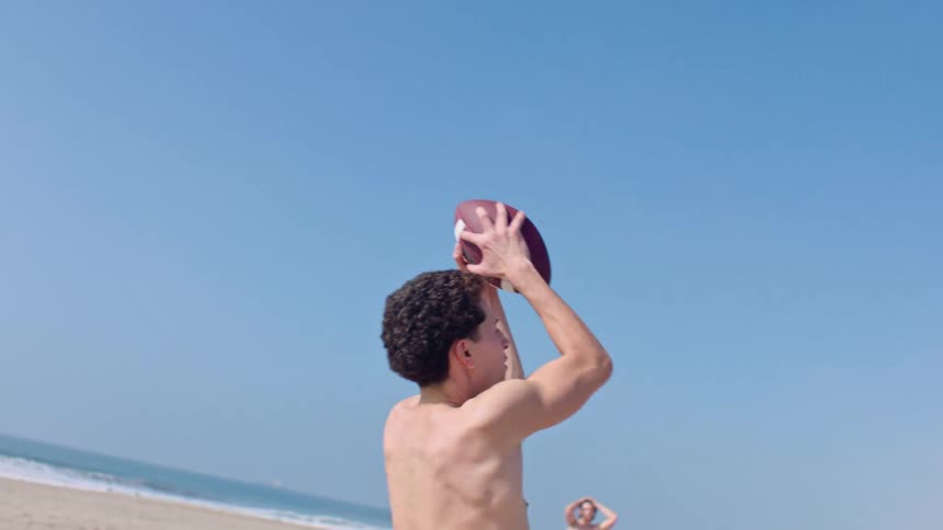 Young man standing on the beach catches a football flying through the air