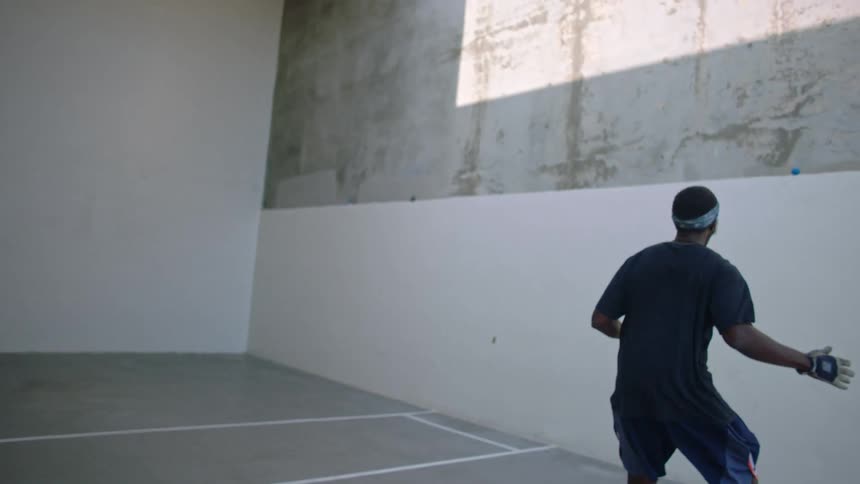 Man wearing a glove is hitting a small ball against a white wall