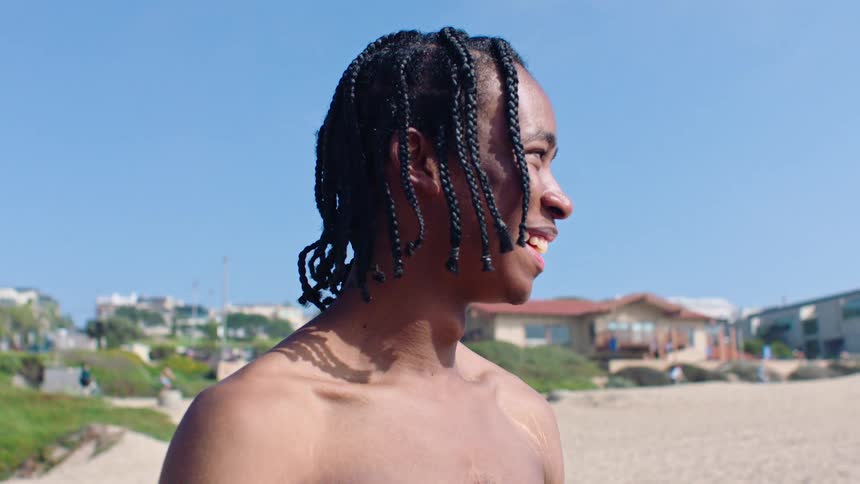 Teenage boy smiles while standing on the beach bordering a residential neighborhood