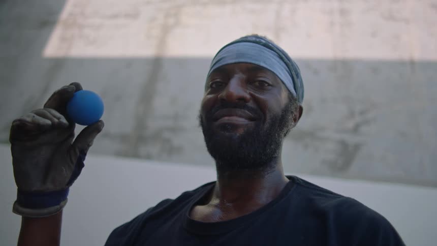 Man standing on a court smiles while holding a handball during the daytime