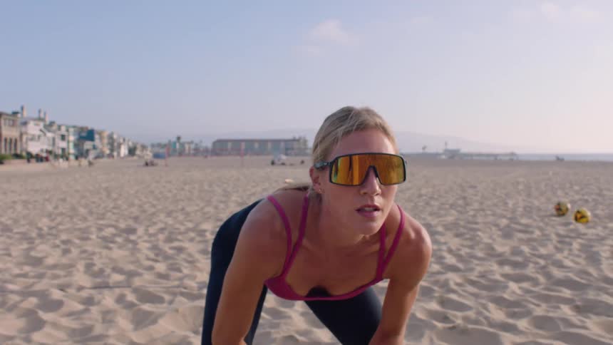 Young woman wearing sunglasses getting into a squat position on the beach at midday