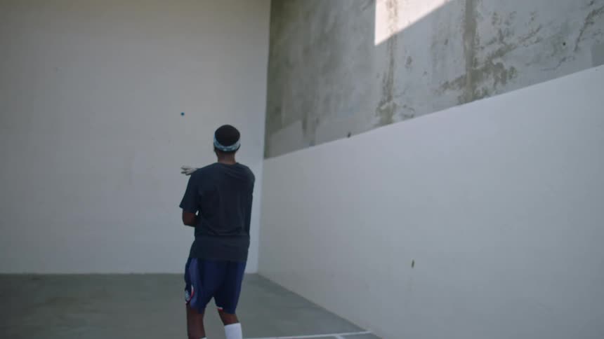 A man strikes a ball against a wall while playing racquetball on an indoor court