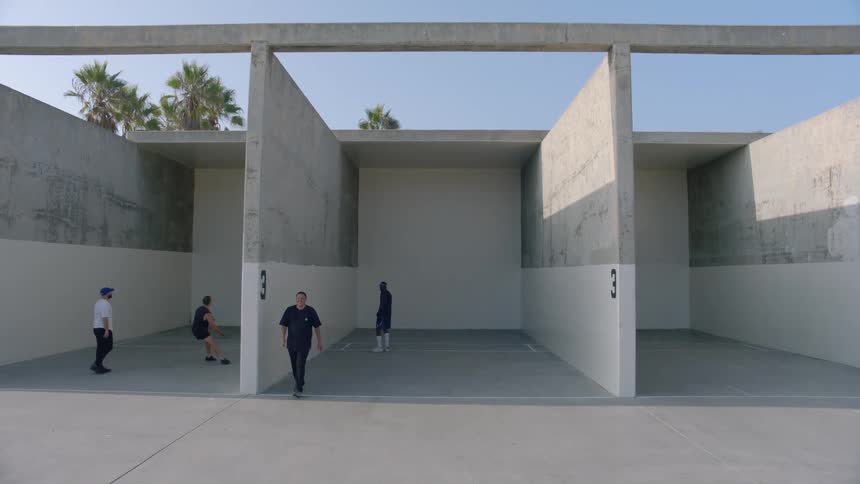 Two pairs throwing a small ball against a wall in an outdoor pavilion