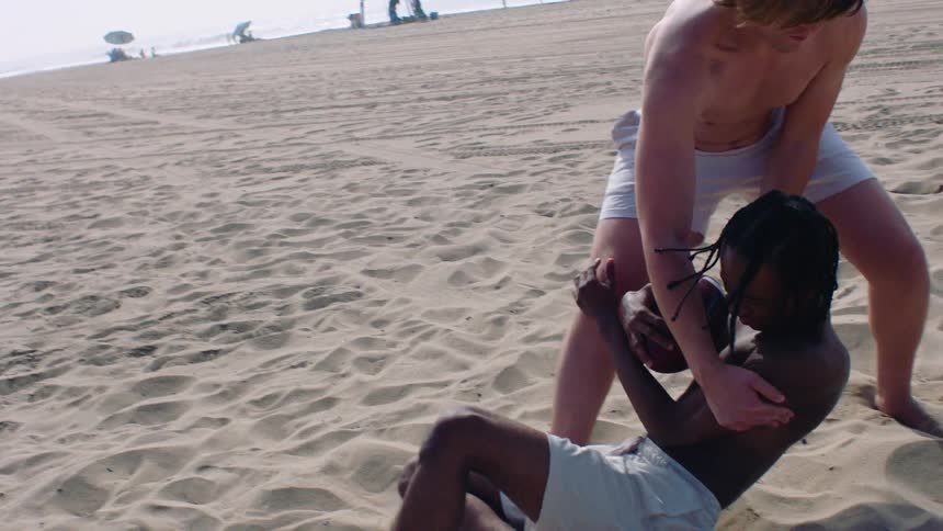 Two male teenagers playing american football outdoors at the beach during daytime