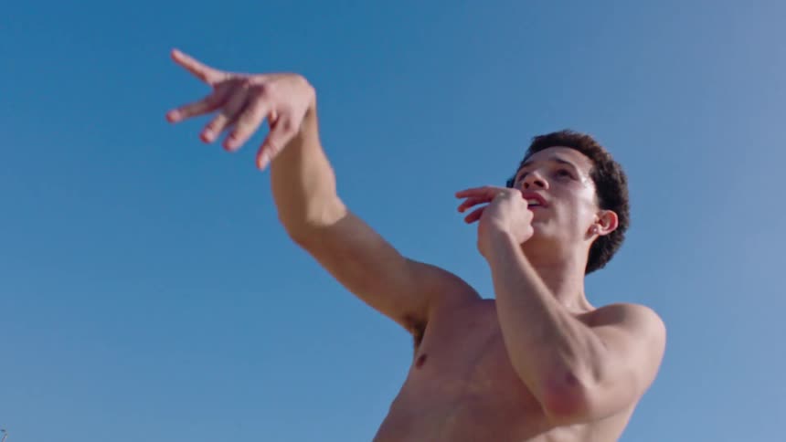 A teenage boy throwing a football outdoors while shirtless