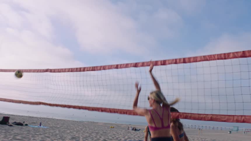 A group of four women are playing volleyball on the sand of a beach and then they greet each other