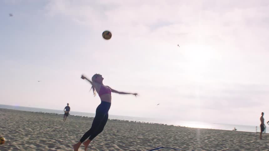 Young women play a volleyball game on the beach on a mostly cloudy day