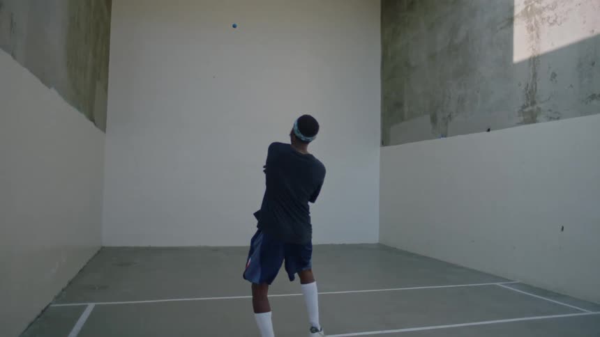 Man wearing a glove is throwing a small ball against a white wall