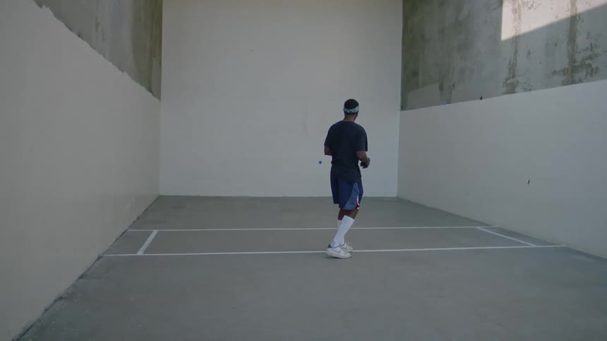 Man plays handball in a concrete walled court