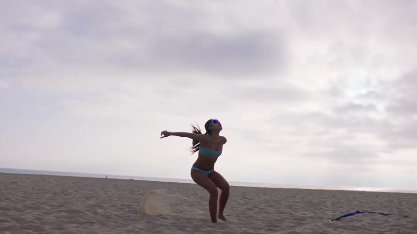 Woman jumps up to serve a volleyball during a game on the beach