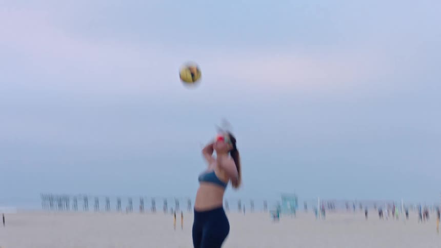 A young woman playing volleyball outdoors at the beach during daytime
