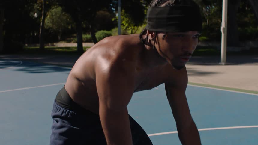 Shirtless man demonstrating basketball skills on an outdoor court