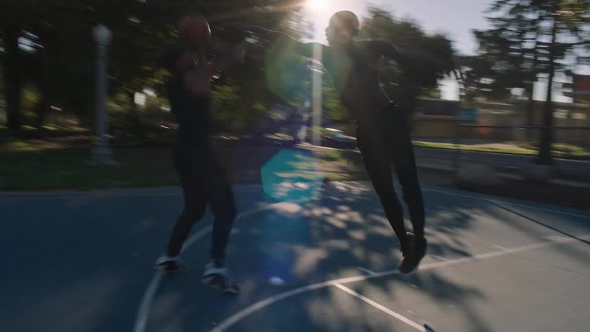 Friends play one on one basketball on a court at the park on a sunny day