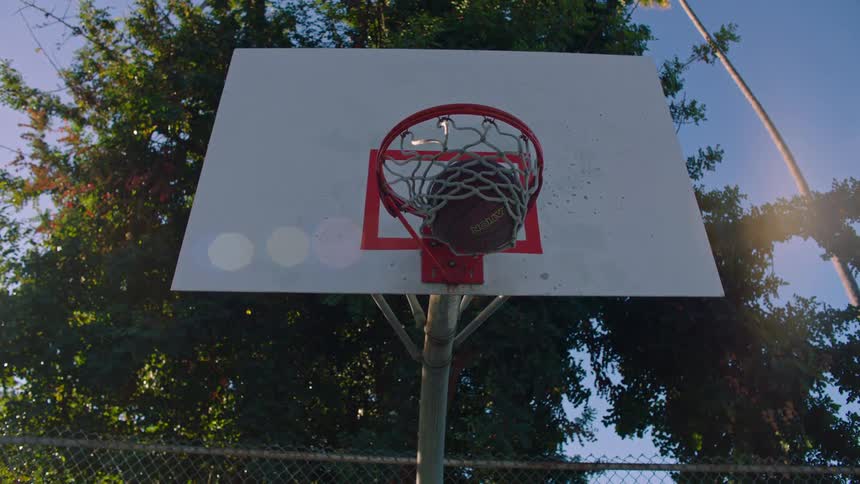 Basketball flies through the air hitting the backboard and falling through the hoop and net