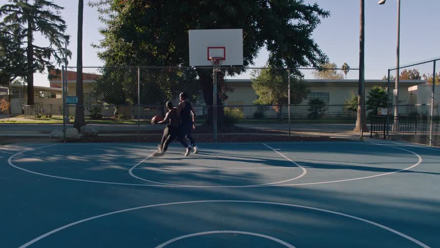 Two men are playing basketball on a blue court and one of them is shooting the ball and making a basket