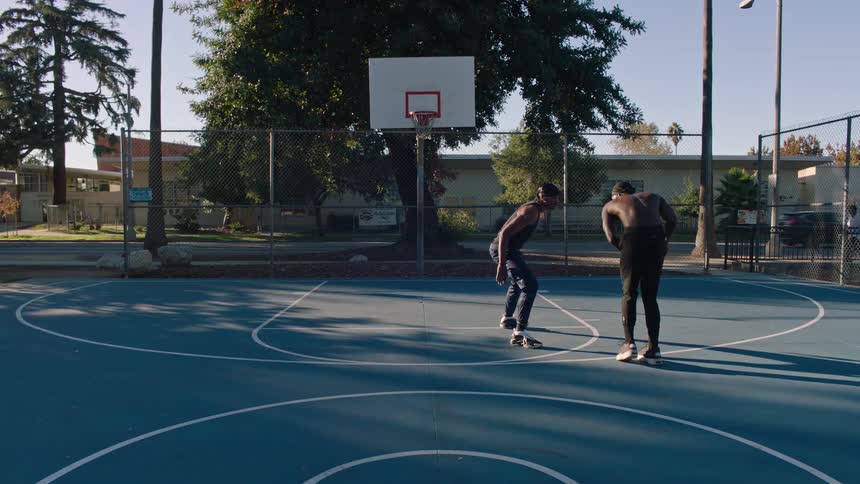 Two men are playing basketball on a blue court and one of them shoots the ball and makes a basket