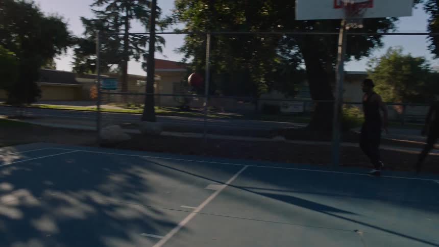 Two men play basketball on a court in the park on a sunny summer day