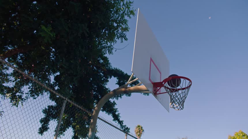 Basketball flies through the air hitting the backboard and falls through the hoop and net