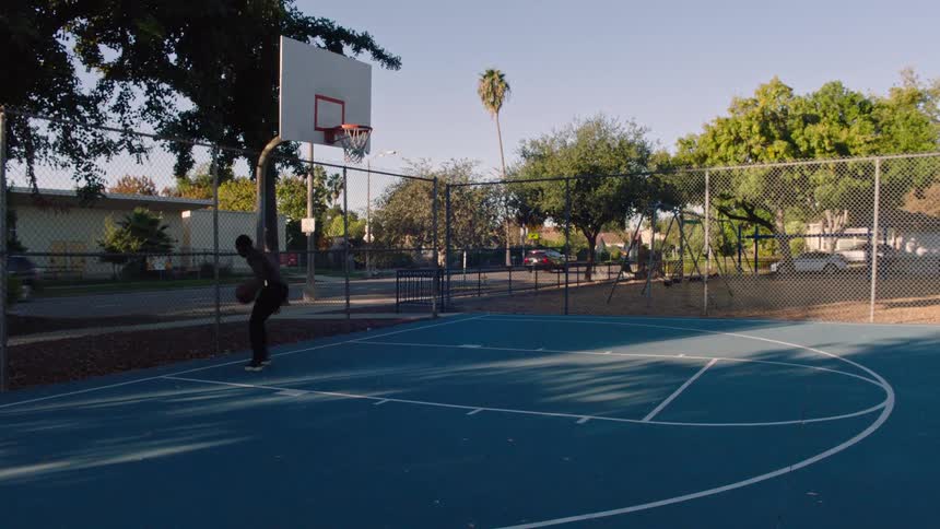 Young black male on an outdoor basketball court dunking the ball into the hoop at midday