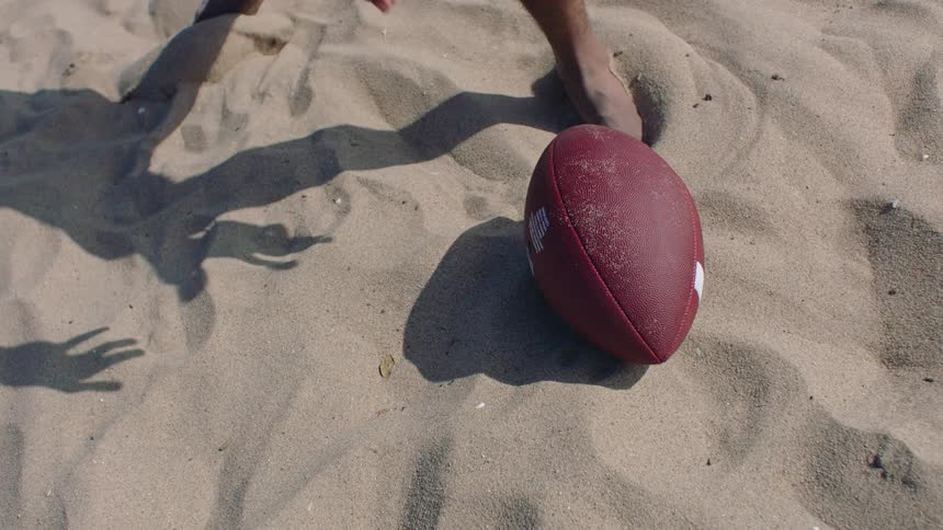 Football lying on the sand at the beach as a person picks it up