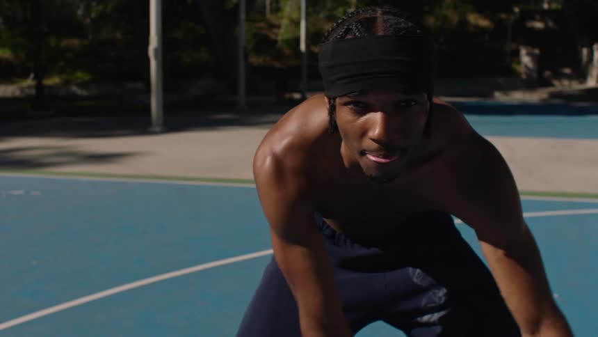 An focused young man prepares to dribble a basketball on a sun drenched outdoor court