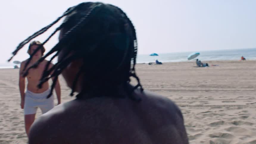 Three men playing american football on the beach sand