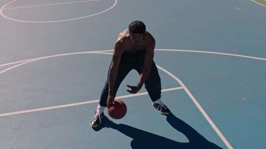 A young black male athlete playing basketball at an outdoor court during daytime
