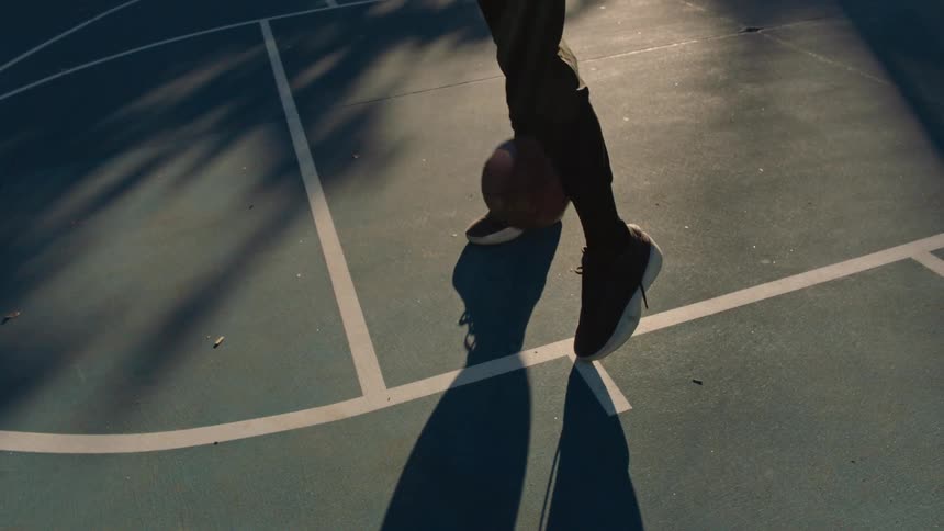 Man standing on the basketball court bounces the basketball between his legs