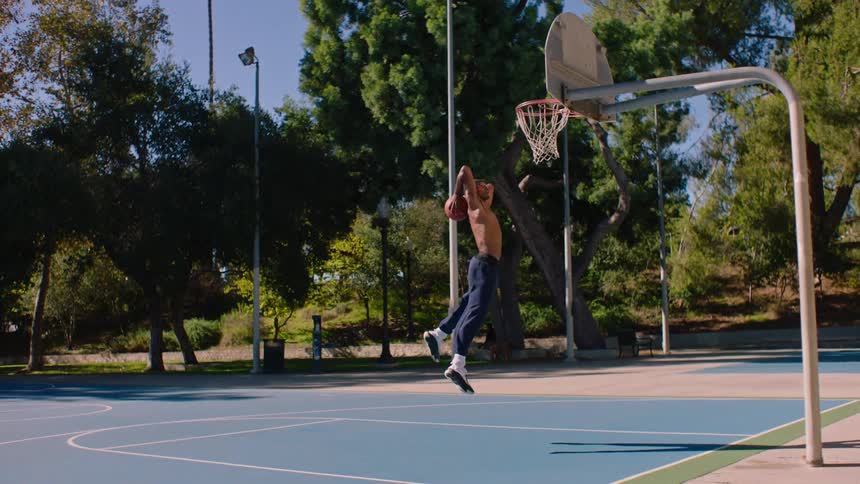 Young man bounces the basketball on the court and jumps to dunk the ball in the basket and holds on to the hoop