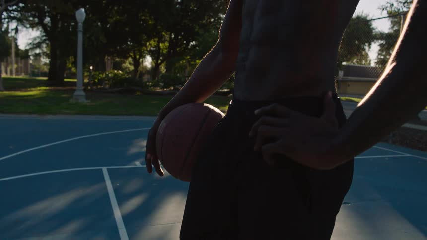 Man on an outdoor court holding a basketball around his waist