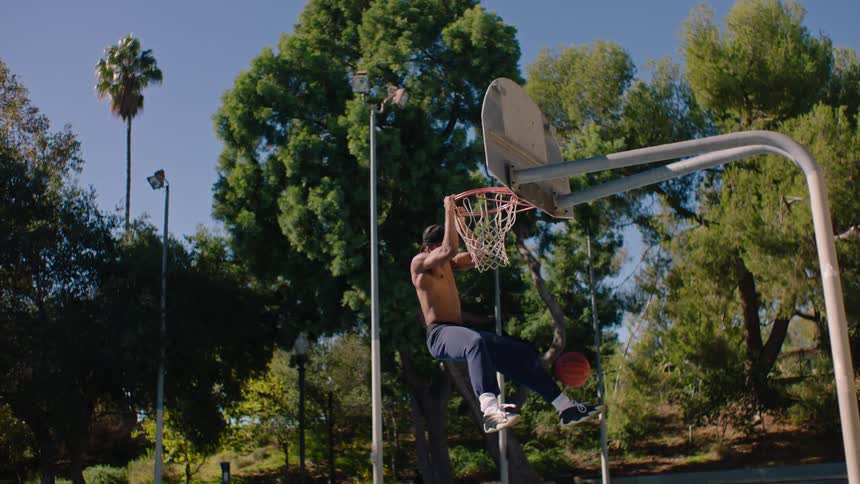 Young man playing basketball jumps and dunks the ball in the basket and holds on to the hoop
