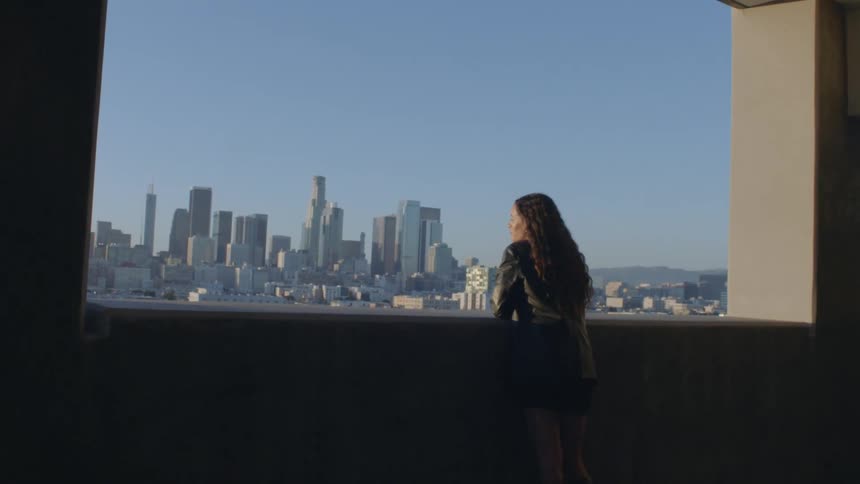 Woman standing near a window looks at the city skyline on a sunny day