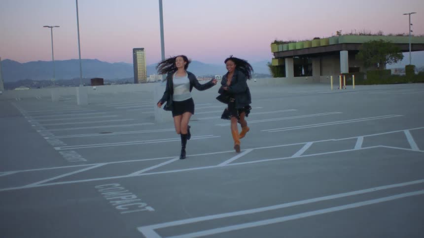 Two women with happy expressions running in an outdoor parking lot