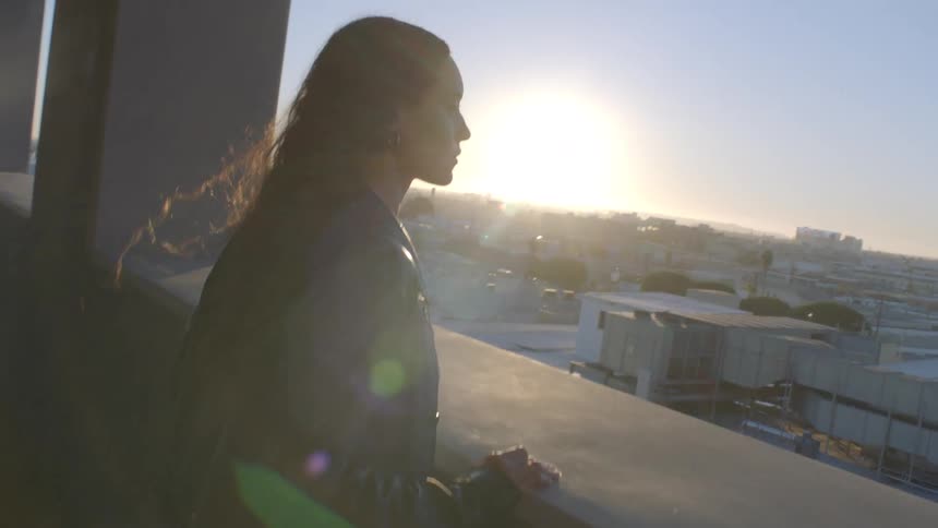 Close up portrait of a young woman standing at a balcony in a city at sunset