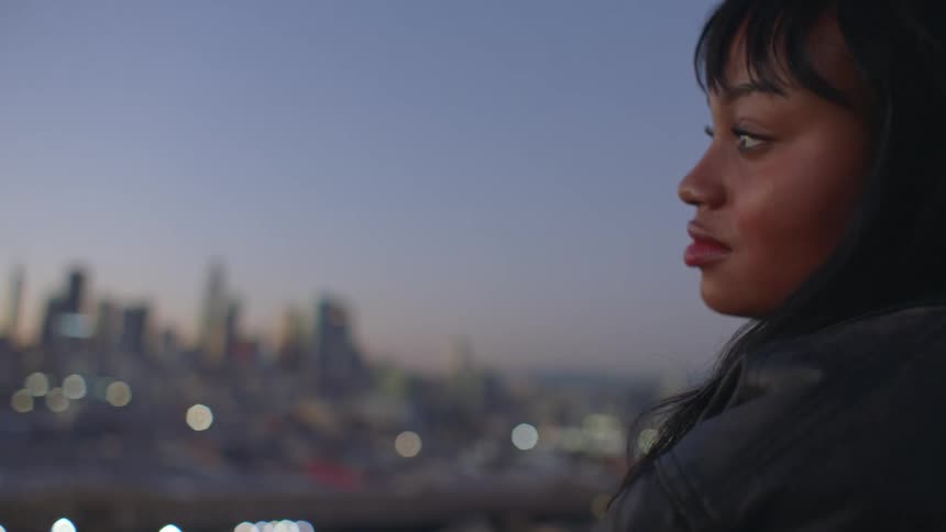 Young woman standing on a balcony at sunrise gazing out over the city as the early light warms the skyline