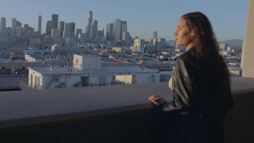 Woman standing on a balcony looking over an urban skyline with buildings in the background during daytime