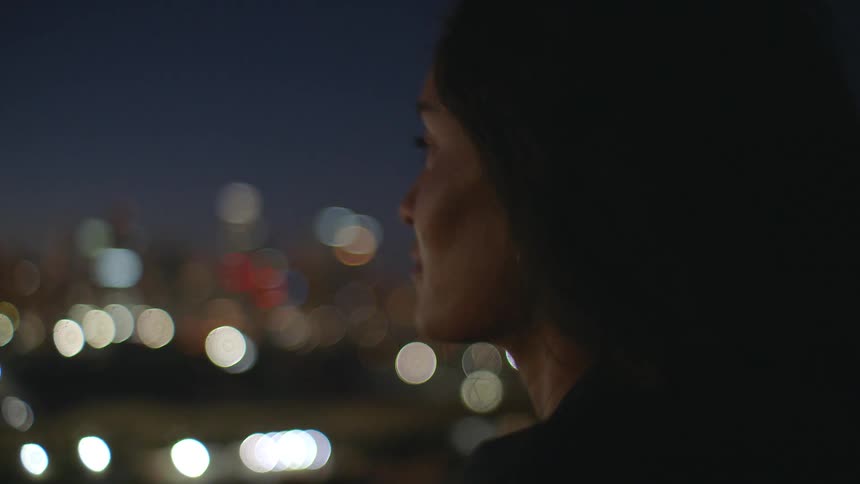 Close up portrait of a young black woman standing on a rooftop in a metropolitan city at night