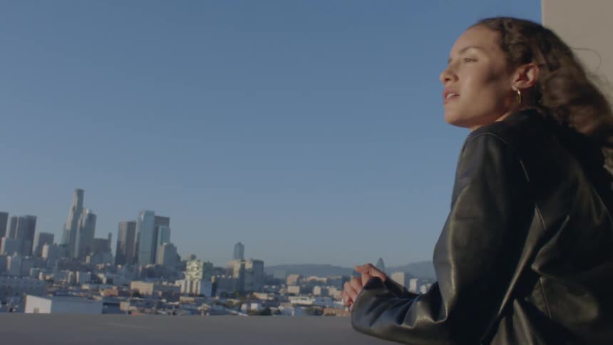 Young woman resting on the balcony of a highrise building at sunrise watching the city skyline glowing in the early light