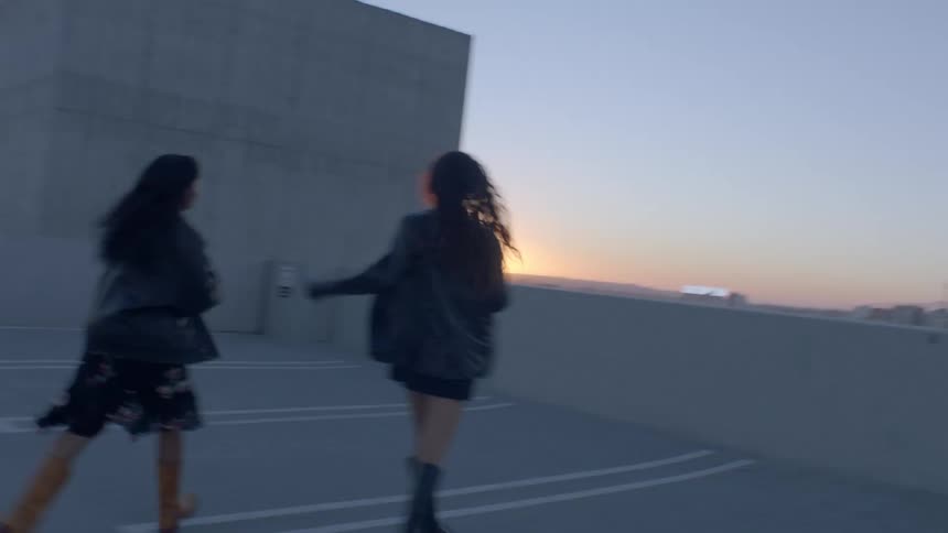 Two women are strolling in an openair parking lot gazing at the horizon