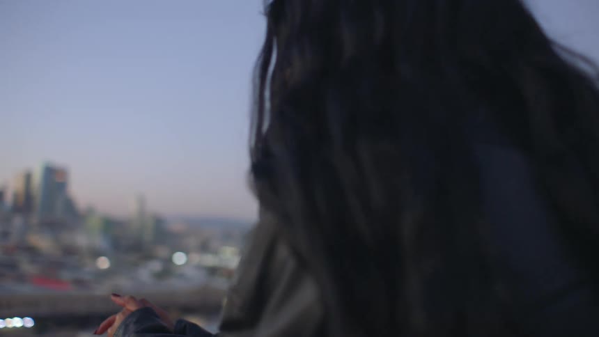 Friends smile at each other while standing on a balcony and looking at the city after dusk