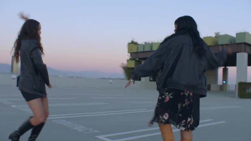 Two young girls are dancing happily in a parking lot