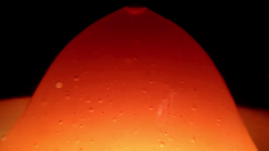 Closeup of a glowing orange liquid dome with tiny bubbles against a dark background
